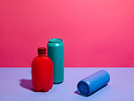 Still life of turquoise and blue drink cans with red bottle and pink background