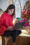 Young woman in red sweater on living room sofa looking at laptop