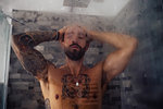 Mid adult man with tattooed chest in shower