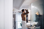 Mid adult man with tattoos combing hair at bathroom mirror