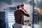 Mid adult man with tattoos combing hair at bathroom mirror