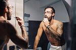 Mid adult man with tattoos brushing teeth at bathroom mirror