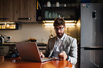 Mid adult man sitting at kitchen table with laptop and credit card