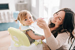 Mother feeding baby daughter in child seat, portrait