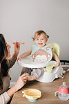 Mother feeding baby daughter in child seat, portrait