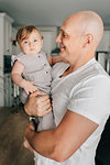 Father carrying baby daughter in living room, portrait