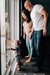 Mother and father with baby daughter looking out through patio door