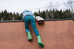 Boy clambering to top of skateboard ramp, rear view