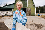 Blond boy carrying skateboard in farmyard, portrait