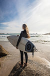 Young female surfer looking out from beach, rear view, Cape Town, Western Cape, South Africa