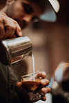 Barista pouring milk into coffee glass in cafe, close up of hands