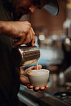 Barista pouring milk into cup of latte in cafe, close up of hands