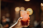 Barista holding up glass of fresh iced fruit juice in cafe, close up of hand
