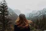 Young woman shaking long brown hair in mountain landscape, rear view, Yosemite Village, California, USA