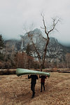 Young canoeing couple carrying canoe over heads in mountain landscape, Yosemite Village, California, USA