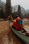 Young canoeing couple pushing off from riverbank, Yosemite Village, California, USA