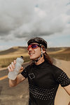 Young male cyclist holding water bottle on rural road, Exeter, California, USA