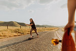 Young barefoot male skateboarder skateboarding on rural road, girlfriend watching, Exeter, California, USA