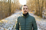 Young man wearing green puffer jacket on snowy road through forest