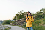 Girl wearing yellow coat using smart phone in park