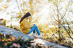 Girl wearing yellow raincoat using smart phone by sea