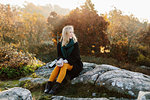 Woman holding mug sitting on rocks by bushes