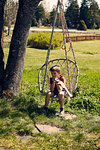 Boy sitting on chair hanging from tree