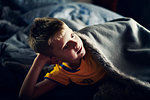 Boy lying under blanket on bed