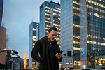 Young man holding cell phone walking down city street