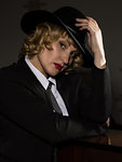 Elegant woman in business suit with a hat poses on a dark background, stylized retro portrait.