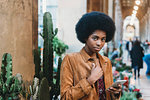 Young woman with afro hair using smartphone in city