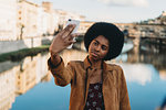 Young woman with afro hair taking selfie by canal, Florence, Toscana, Italy