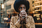 Young woman with afro hair having hot drink in front of cafe