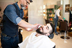 Hairdresser preparing to shave customer's beard in barber shop