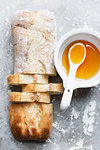 Still life of floured and unfloured ciabatta loaf on baking tray with bowl and spoon, overhead view