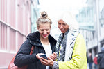 Mature woman and daughter looking at smartphone on city street