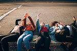 Friends together on kerb taking selfie and using smartphones, Milan, Italy