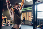 Young tattooed man training in gym, hanging from exercise bar