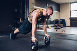 Young tattooed man training in gym, doing push ups on kettle bells