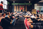 Large group of women training in gym with male trainers, sitting on floor with legs raised