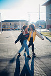 Two cool young female friends strolling and laughing on urban sidewalk