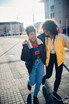 Two cool young female friends laughing on urban sidewalk