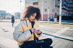 Cool young woman sitting on urban wall untangling earphones