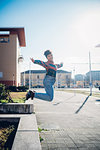 Young woman jumping from wall on urban sidewalk, full length portrait