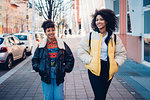 Two cool young women strolling on urban sidewalk