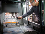 Knife factory worker spraying liquid onto machinery in workshop