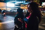 Young woman in hijab and friend on pedestrian crossing in city at night