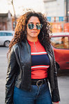 Mid adult woman with long curly hair wearing shades on city sidewalk, portrait