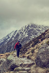 Male hiker hiking in rugged landscape with snow capped mountains, Llanberis, Gwynedd, Wales