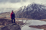 Male hiker looking out at lake and snow capped mountain landscape, Llanberis, Gwynedd, Wales